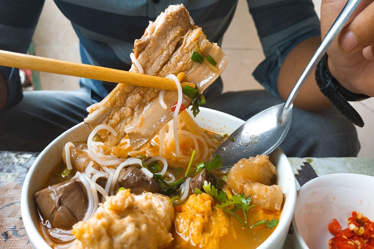 bowl of bún bò Huế with beef, noodles, herbs, and chili broth - top 10 hue food and where to eat in saigon - Jackfruit