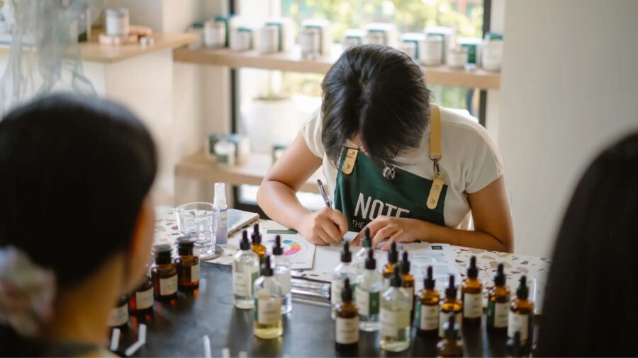 A participant writes down a fragrance formula during a perfume-making workshop, surrounded by essential oils and scent materials.