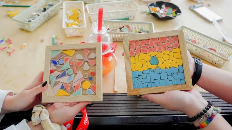 Two finished mosaic artworks with colorful tile patterns are held up at a craft workshop in Ho Chi Minh City.