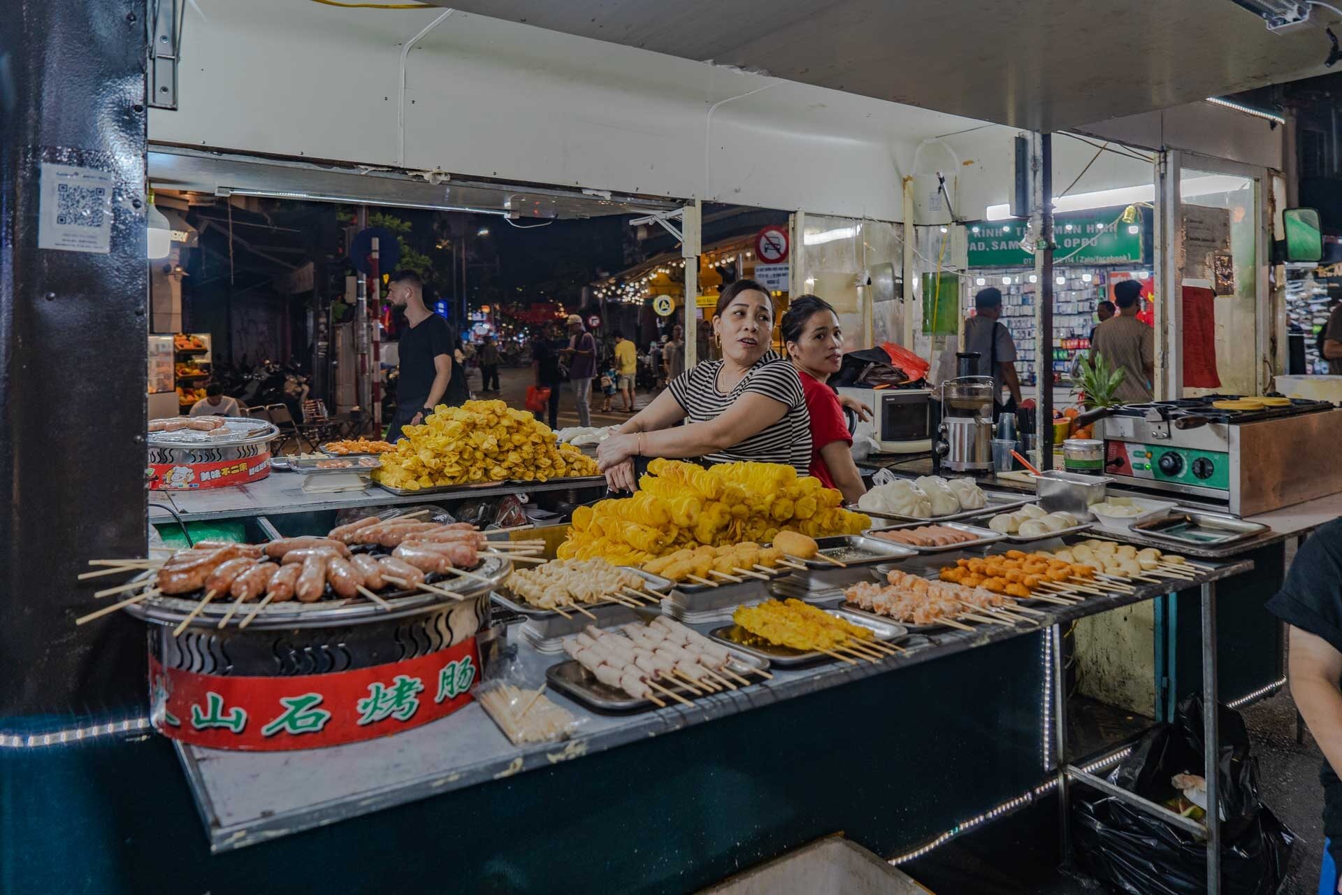 Street food stall with snacks and grilled skewers at the night market Hanoi - Jackfruit Adventure